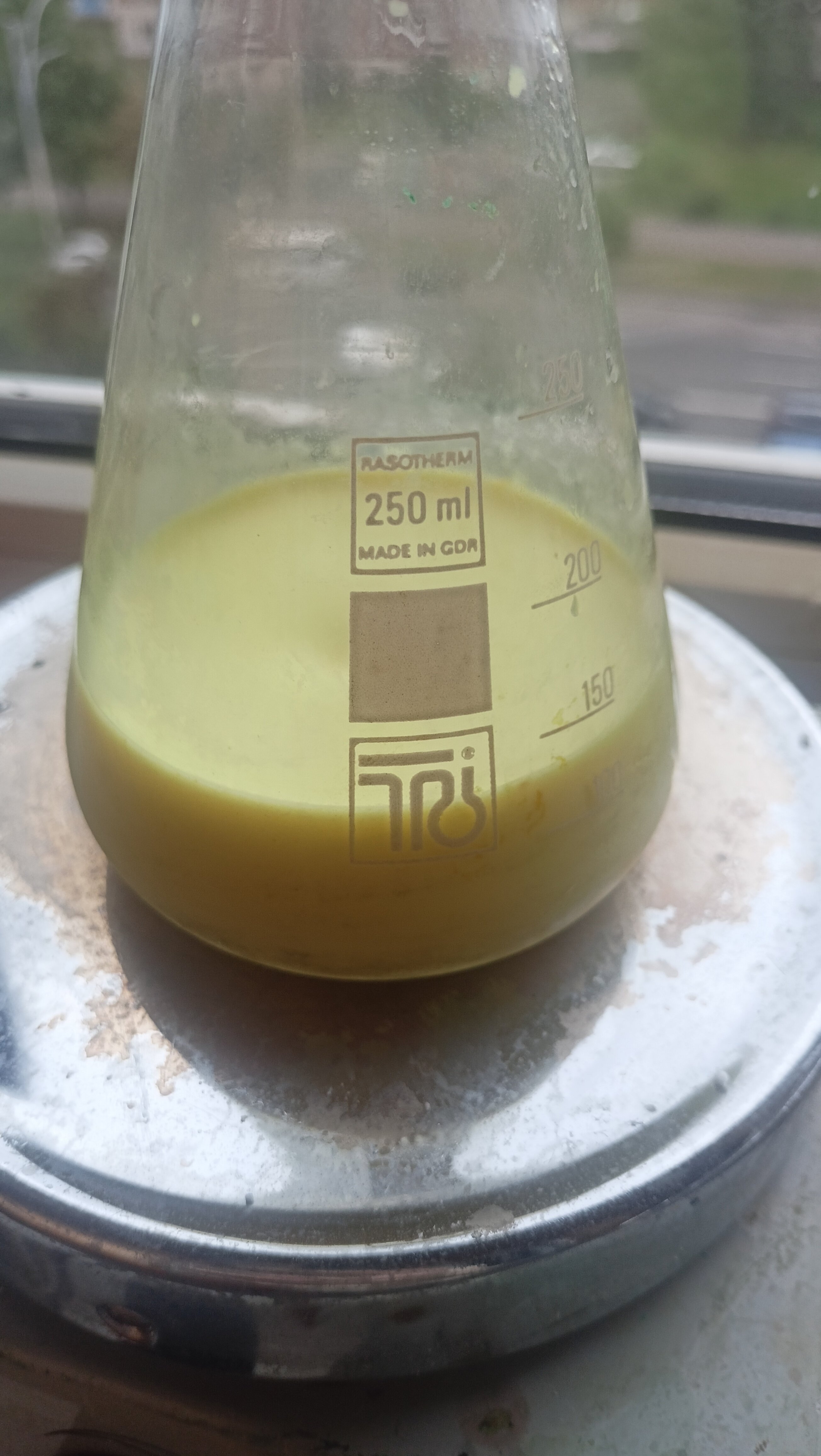 Erlenmeyer flask on a stir plate with a yellow solid in suspesion