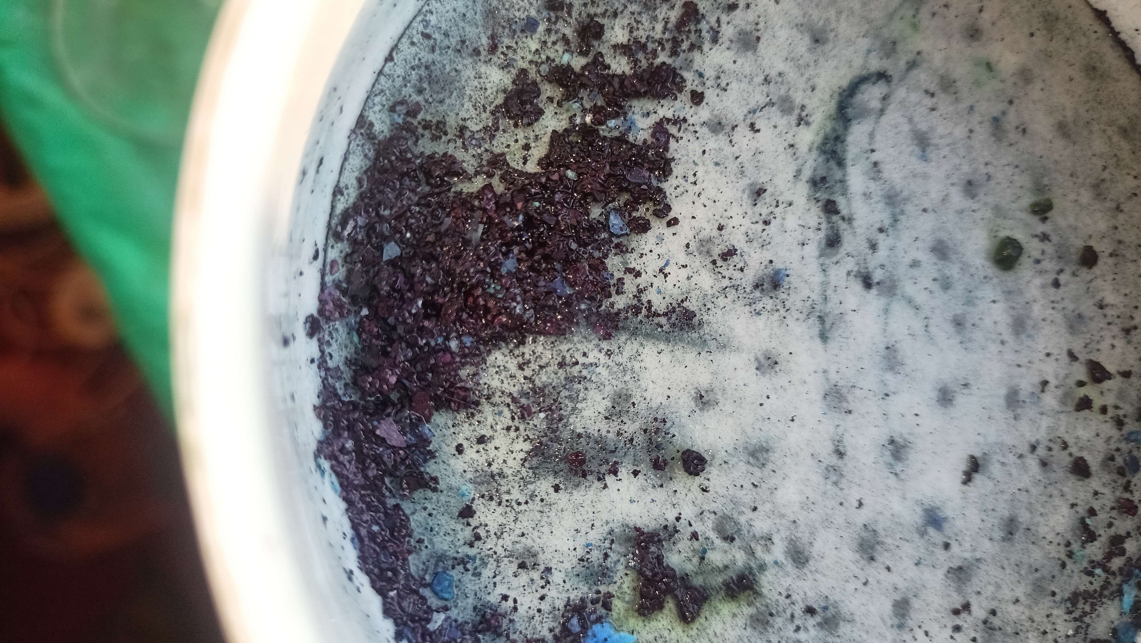 Dark blue crystals in a filter funnel on top of a filter paper with some green stains and blue impurities on it